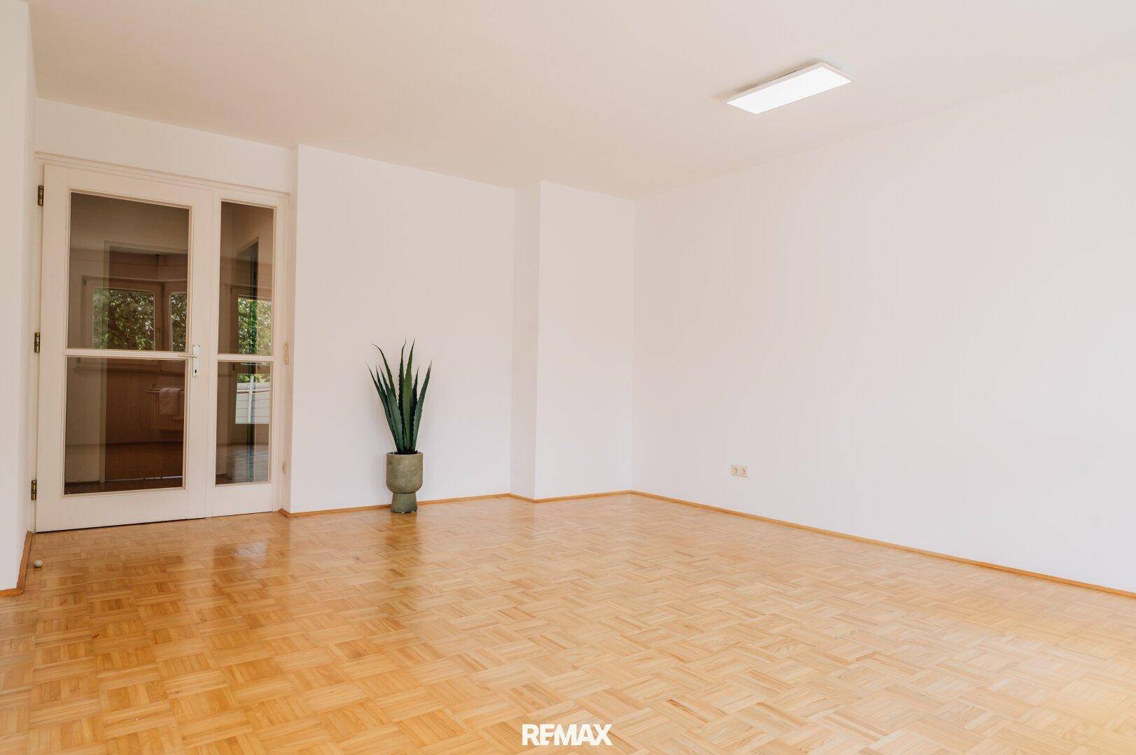 Geräumiges Wohnzimmer mit hellem Parkettboden und viel Tageslicht durch die großen Fenster.