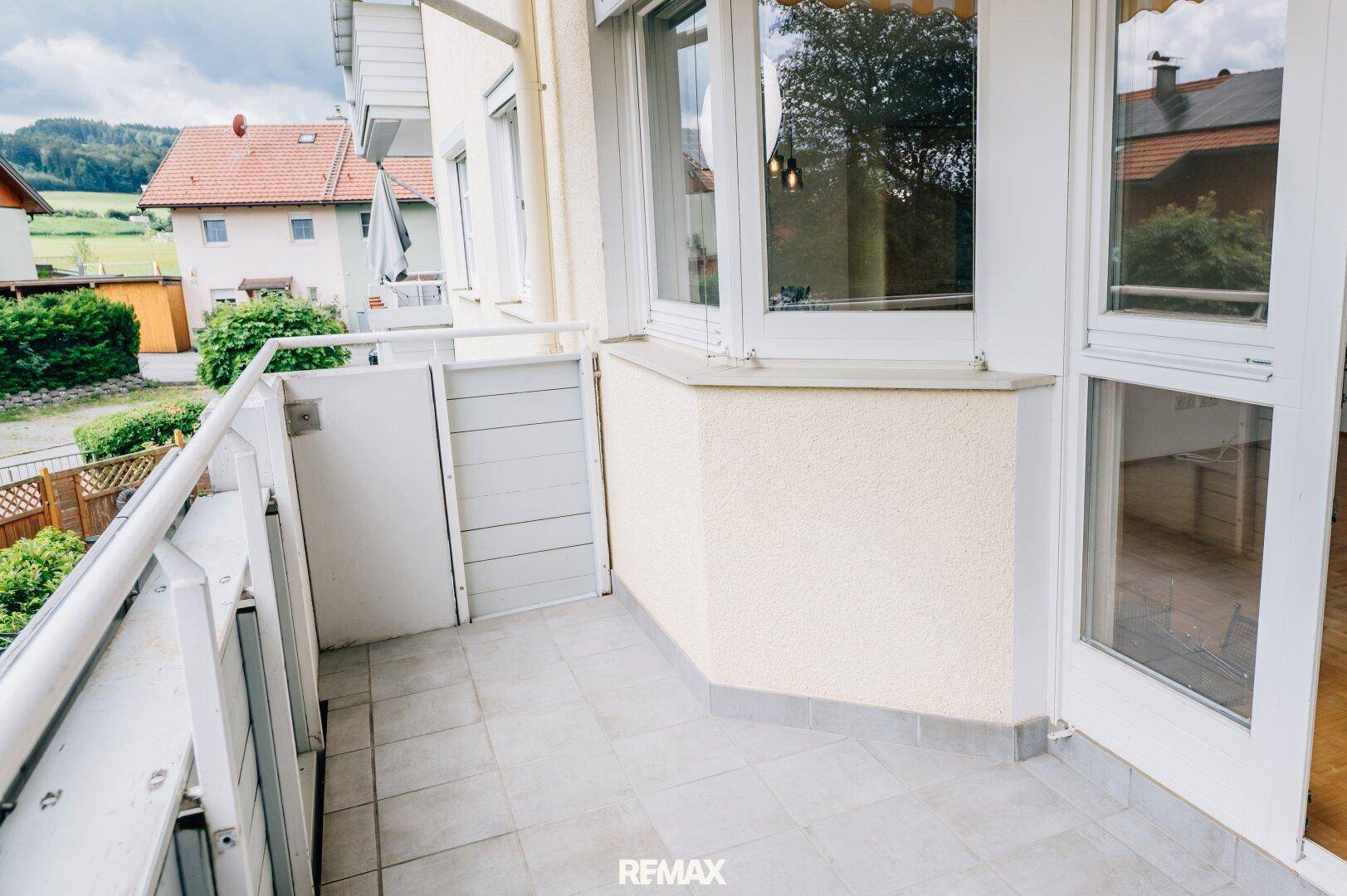 Heller Balkon mit Fliesenboden und Blick auf die umliegenden Häuser und grüne Landschaft.
