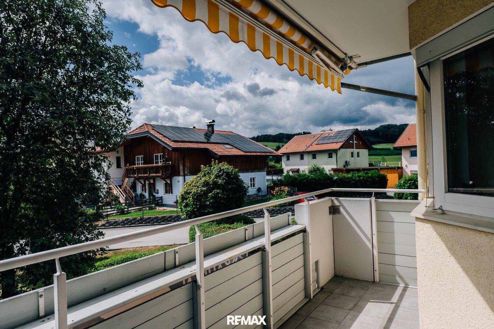 Balkon mit ausziehbarer Markise und weitem Blick auf Häuser mit Solaranlagen und grüne Hügel.