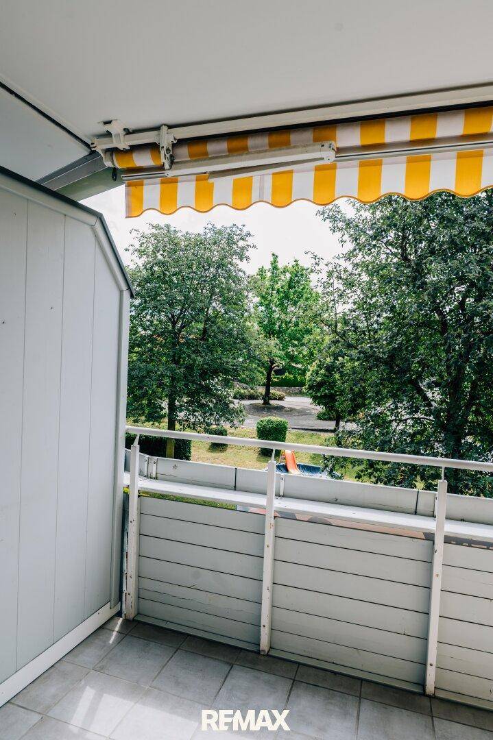 Balkon mit gestreifter Markise und Blick auf den gemeinschaftlichen Gartenbereich mit Spielplatz.