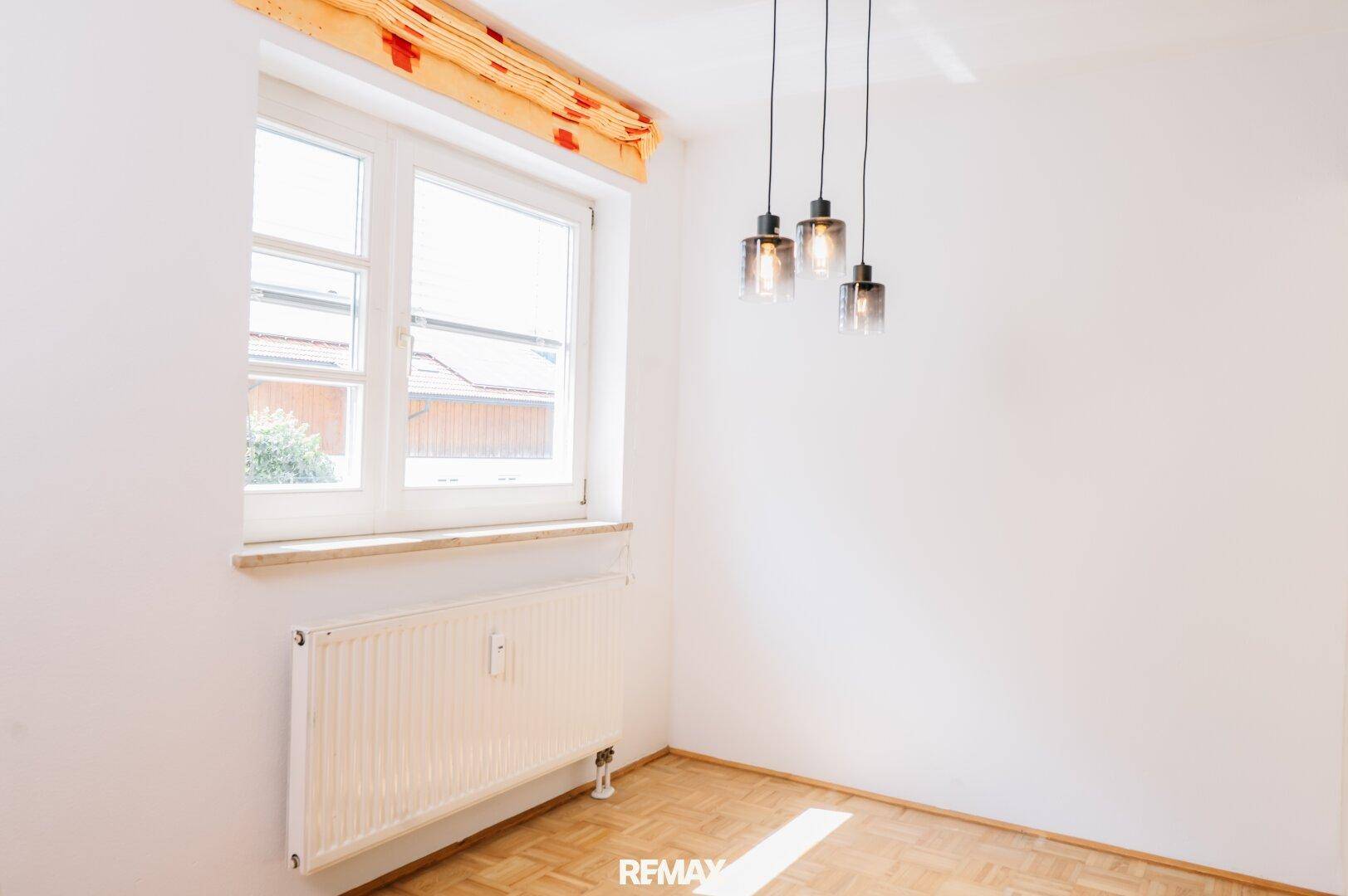 Helles Zimmer mit Parkettboden, weißen Wänden und modernen Hängelampen.