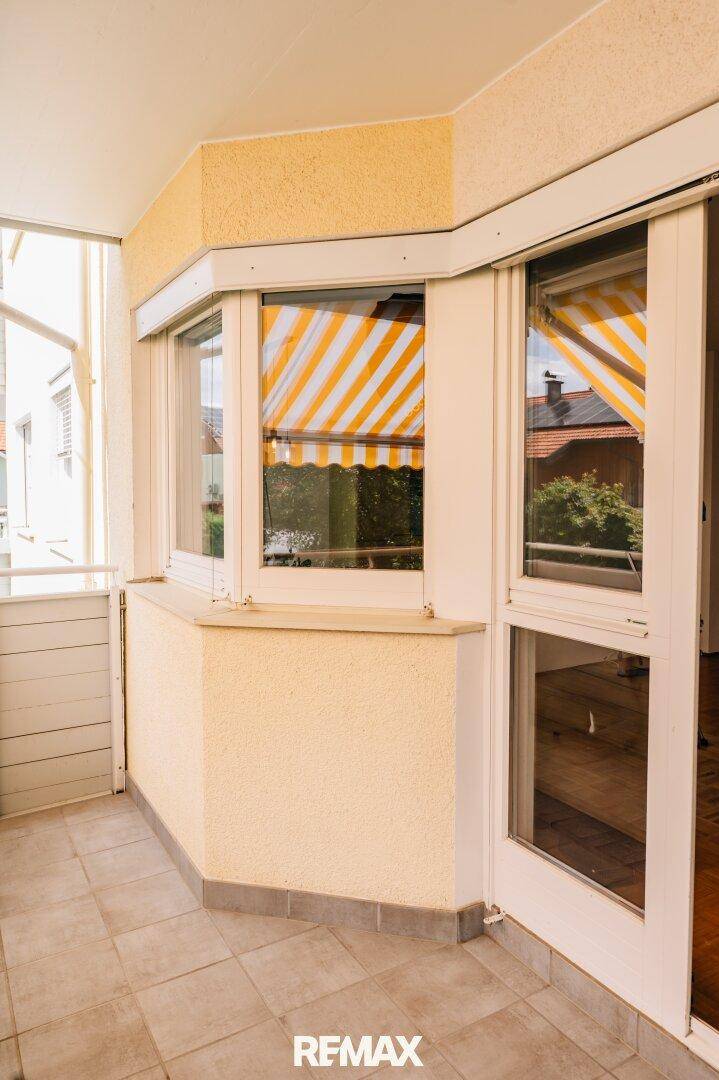 Heller Balkon mit gelben Wänden, Fliesenboden und gestreiften Markisen.