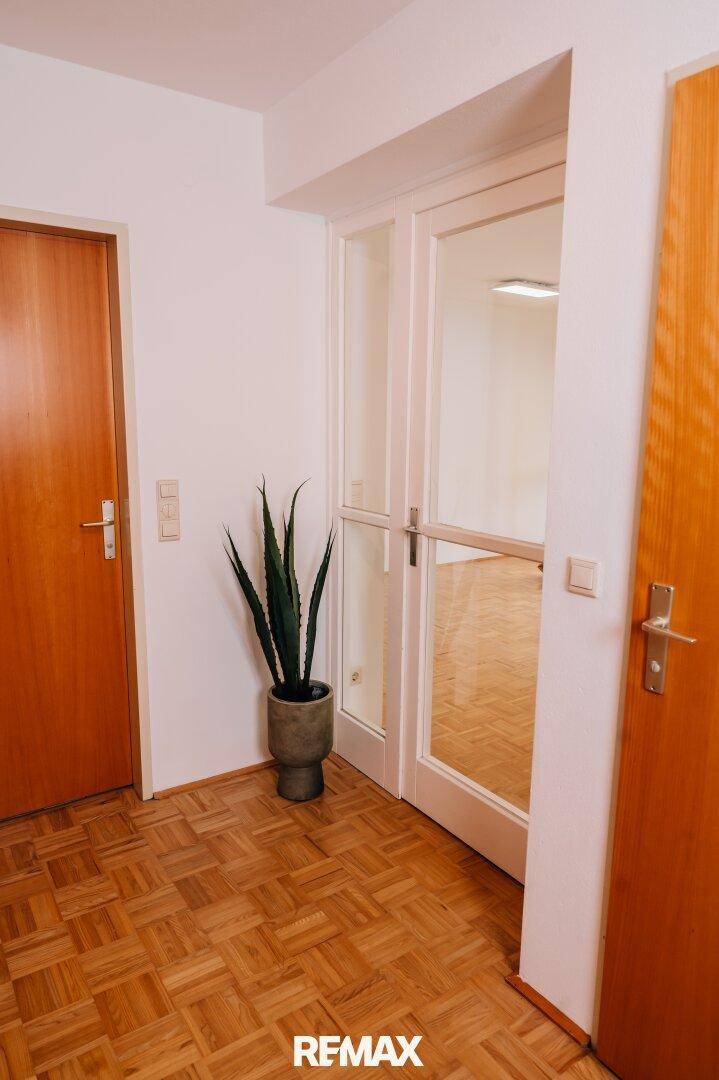 Flur mit Parkettboden, Holztüren und einer Glastür zu einem weiteren Raum.