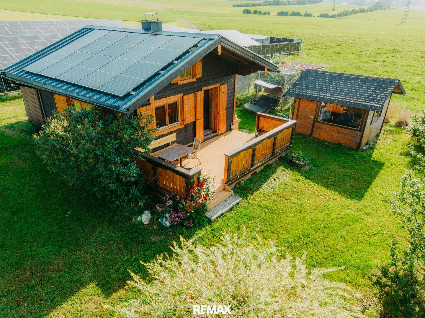 Luftaufnahme des Holzchalets mit Nebengebäude, Solaranlage und weiten Feldern.