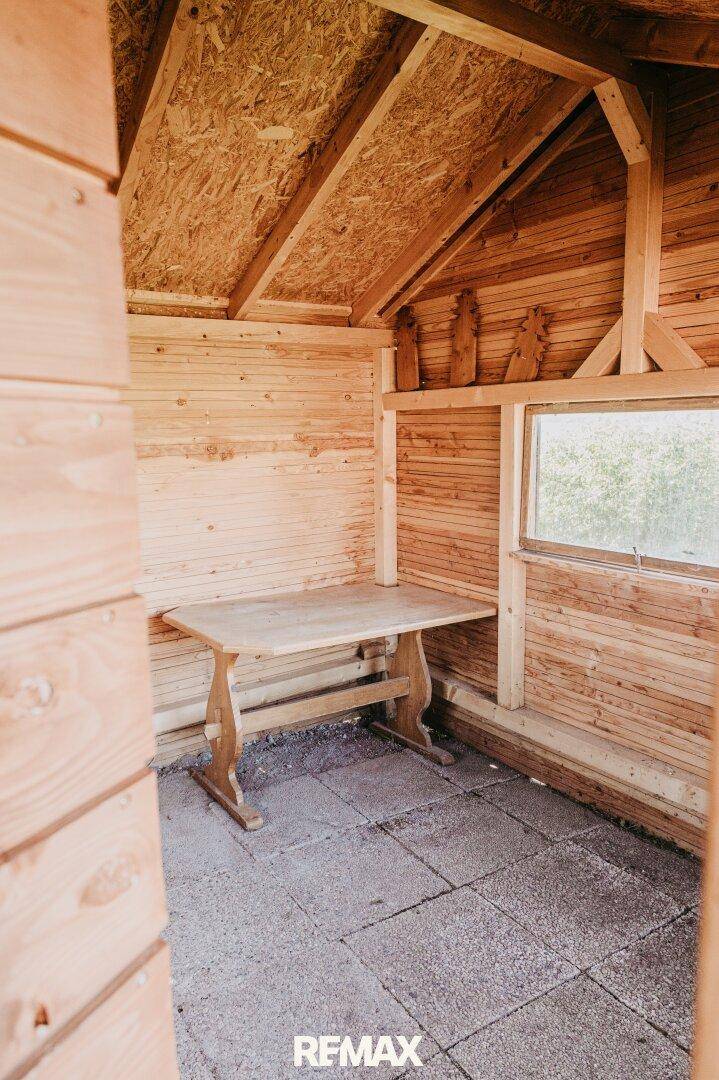 Rustikaler Innenraum eines Holzschuppens mit einfachem Holztisch und Steinboden.