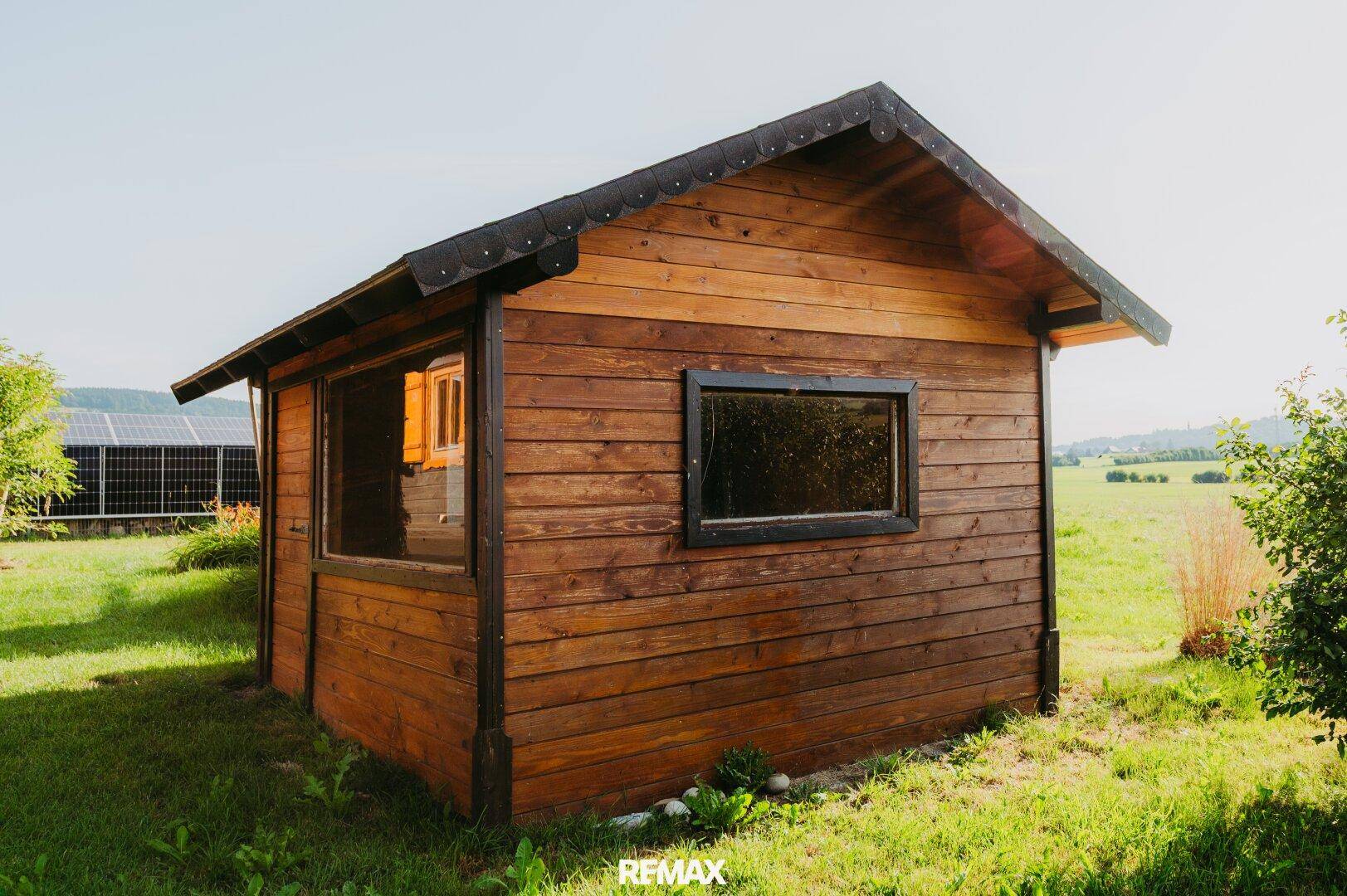 Kleiner Holzschuppen mit Satteldach und Fenstern im Grünen.