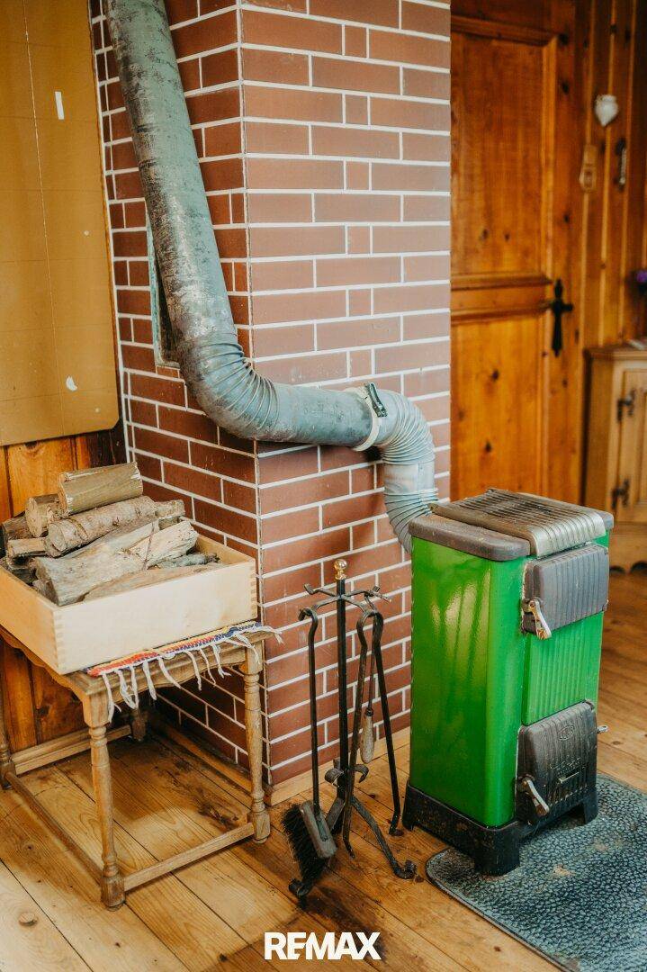 Grüner Holzofen mit Brennholz und Ziegelkamin in einem rustikalen Raum.