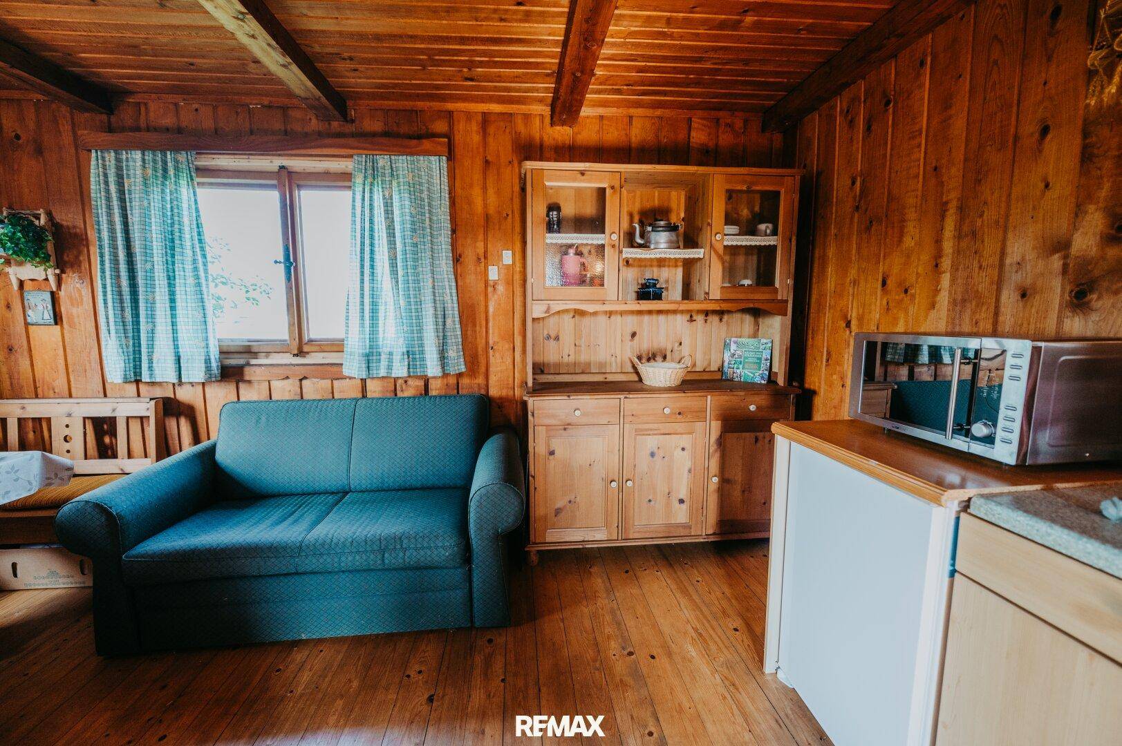 Rustikaler Wohnbereich mit Sofa, Holzschrank und kleiner Küchenzeile.