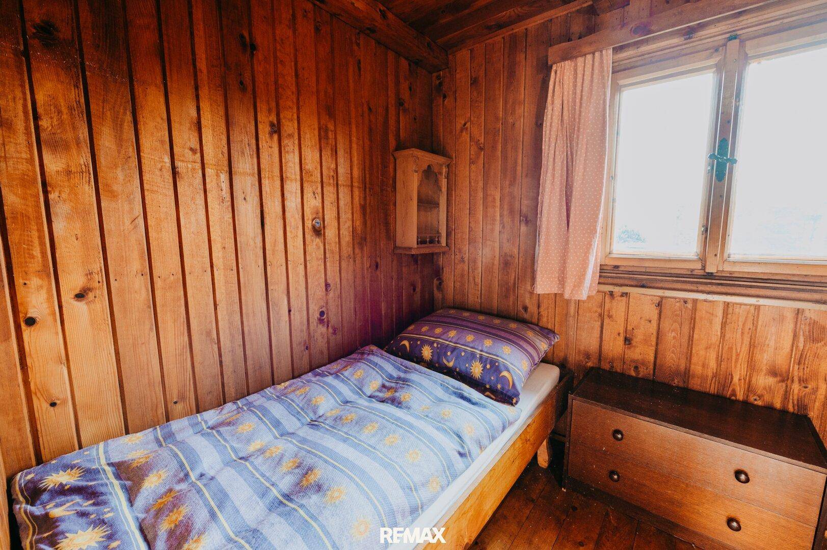 Kleines Schlafzimmer mit Einzelbett und rustikaler Holzvertäfelung.