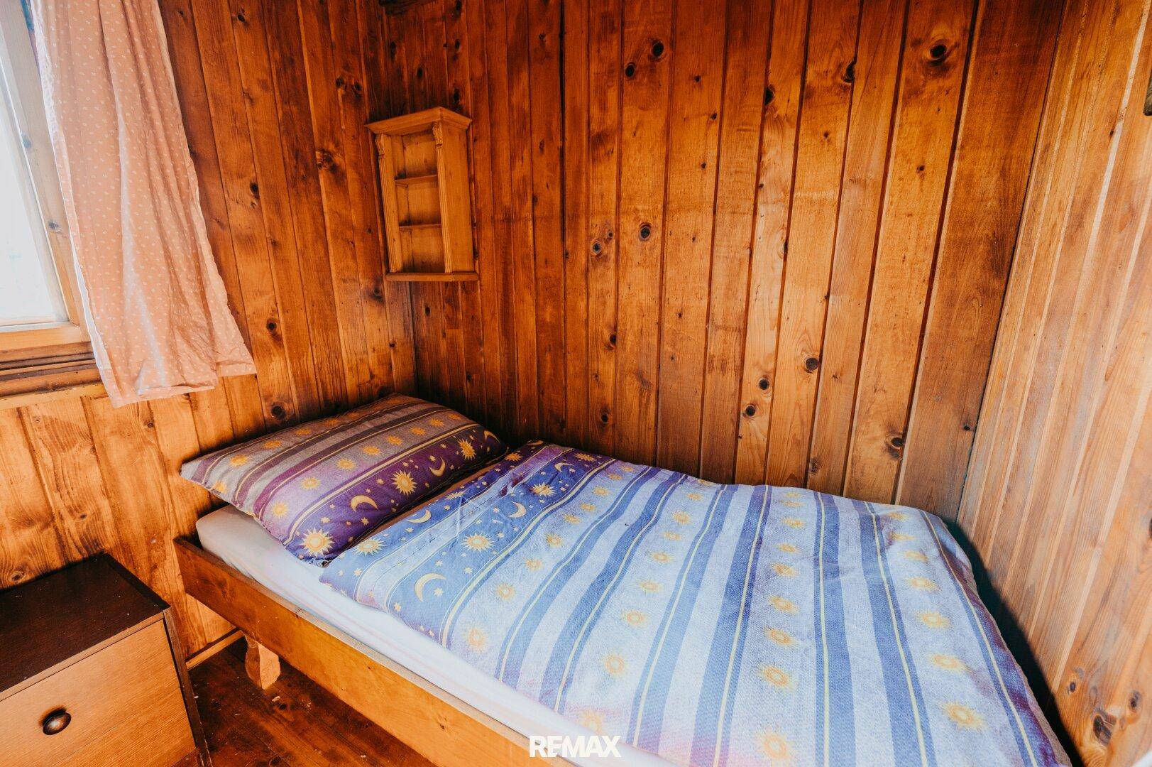 Schlafzimmer mit Einzelbett, Holzvertäfelung und einfacher Einrichtung.