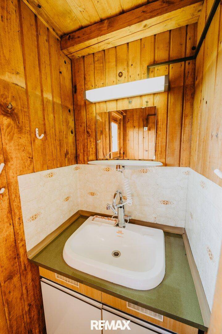 Kleines Badezimmer mit Waschbecken, Spiegel und gefliestem Spritzschutz.