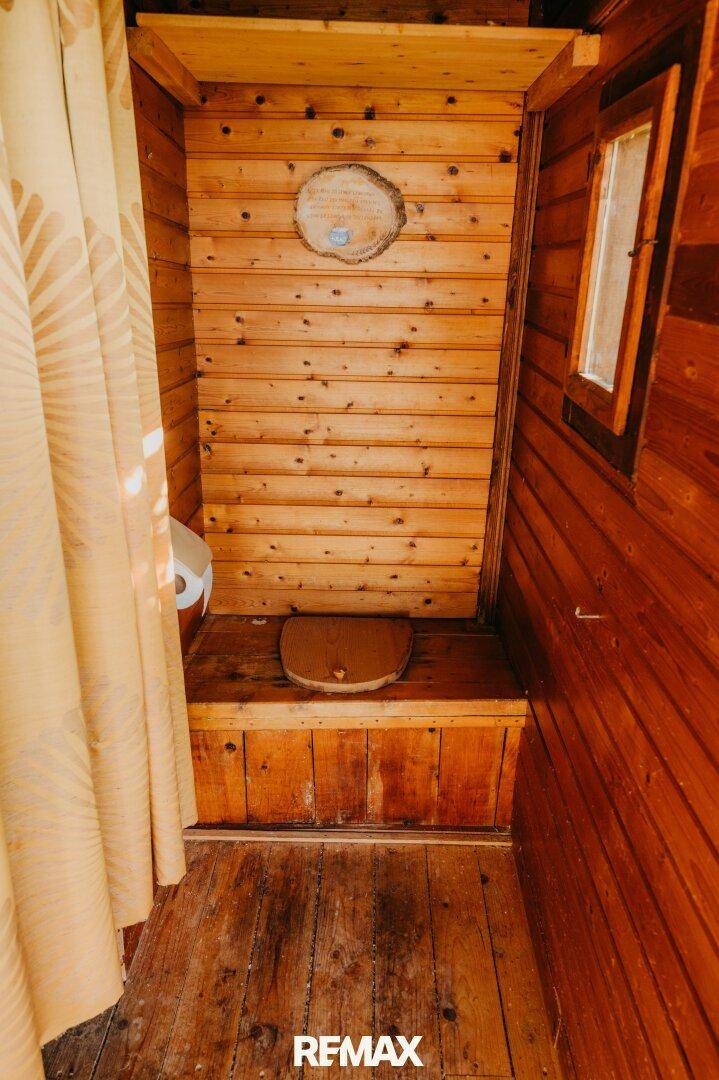 Rustikaler Toilettenbereich mit Holzvertäfelung und kleinem Fenster.