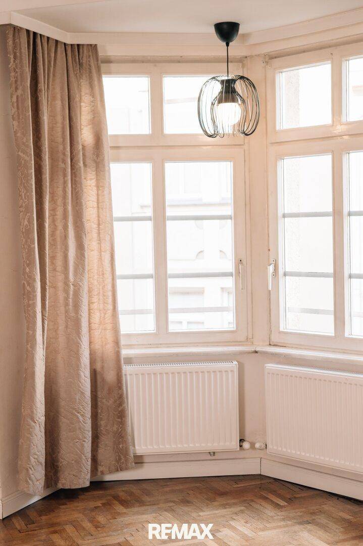Detailansicht der großen Erkerfenster mit Heizkörpern und Vorhängen.