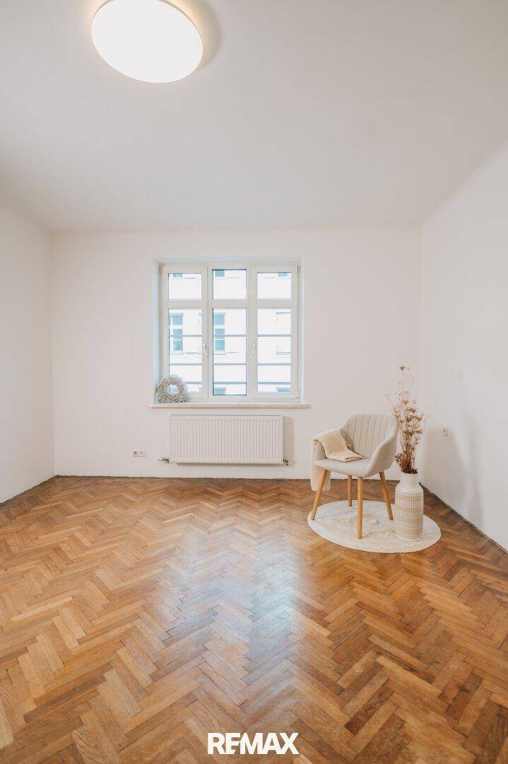 Helles Zimmer mit Fischgrätparkett und großem Fenster, bereit zur individuellen Gestaltung.