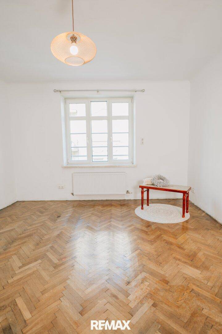 Lichtdurchflutetes Zimmer mit Fischgrätparkett und einem großen Fenster.
