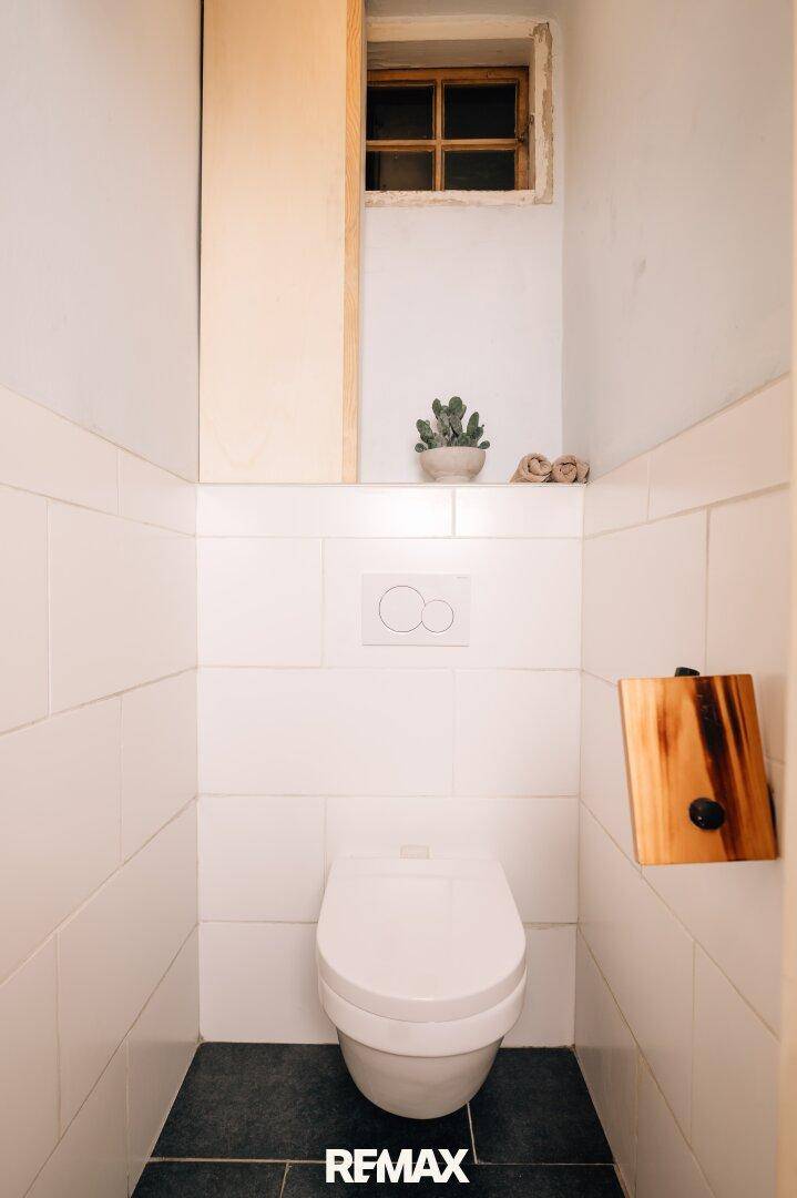 Separates WC mit Wand-WC, Fliesen und kleinem Fenster.