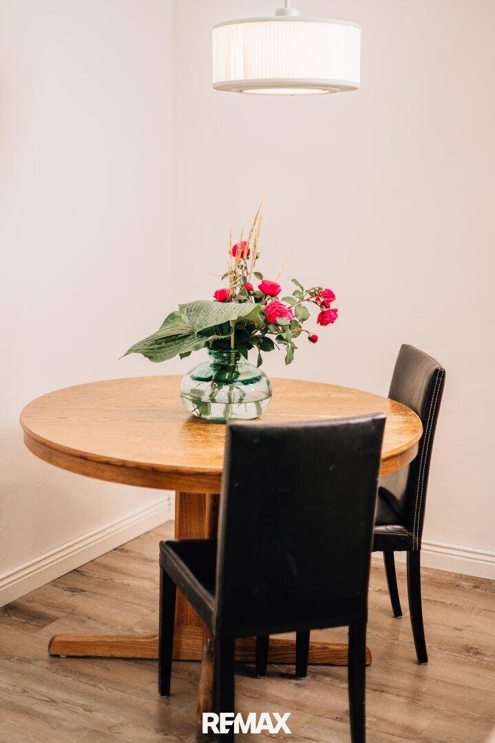 Essbereich mit rundem Holztisch und Blumenarrangement unter einer modernen Pendelleuchte.