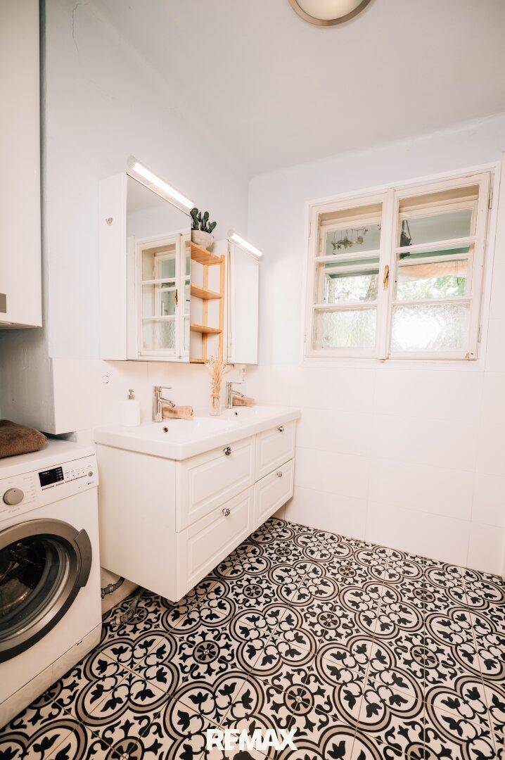 Geräumiges Badezimmer mit Doppelwaschbecken, Waschmaschine und Fenster.