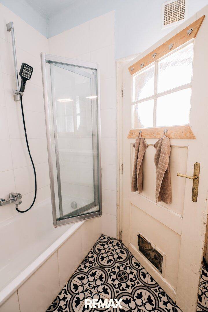 Badezimmer mit Badewanne, Duschvorrichtung und gemusterten Bodenfliesen.