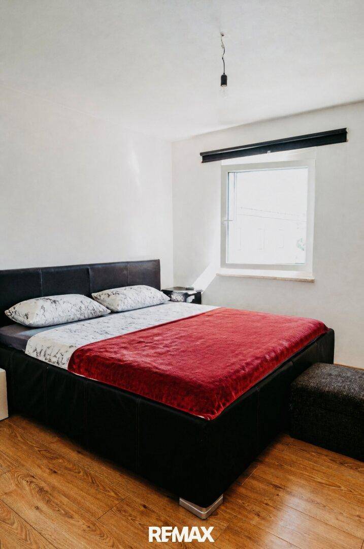 Schlafzimmer mit Doppelbett, Laminatboden und Fenster, das viel Tageslicht hereinlässt.