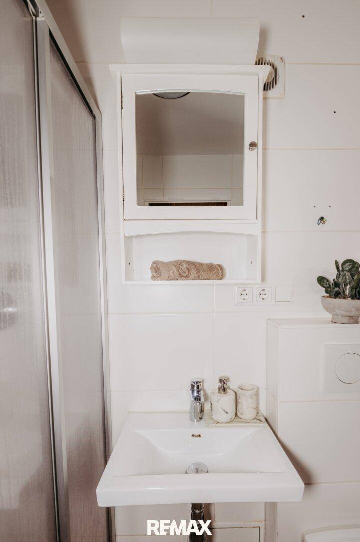 Modernes Badezimmer mit Waschbecken, Spiegelschrank und weißen Fliesen.