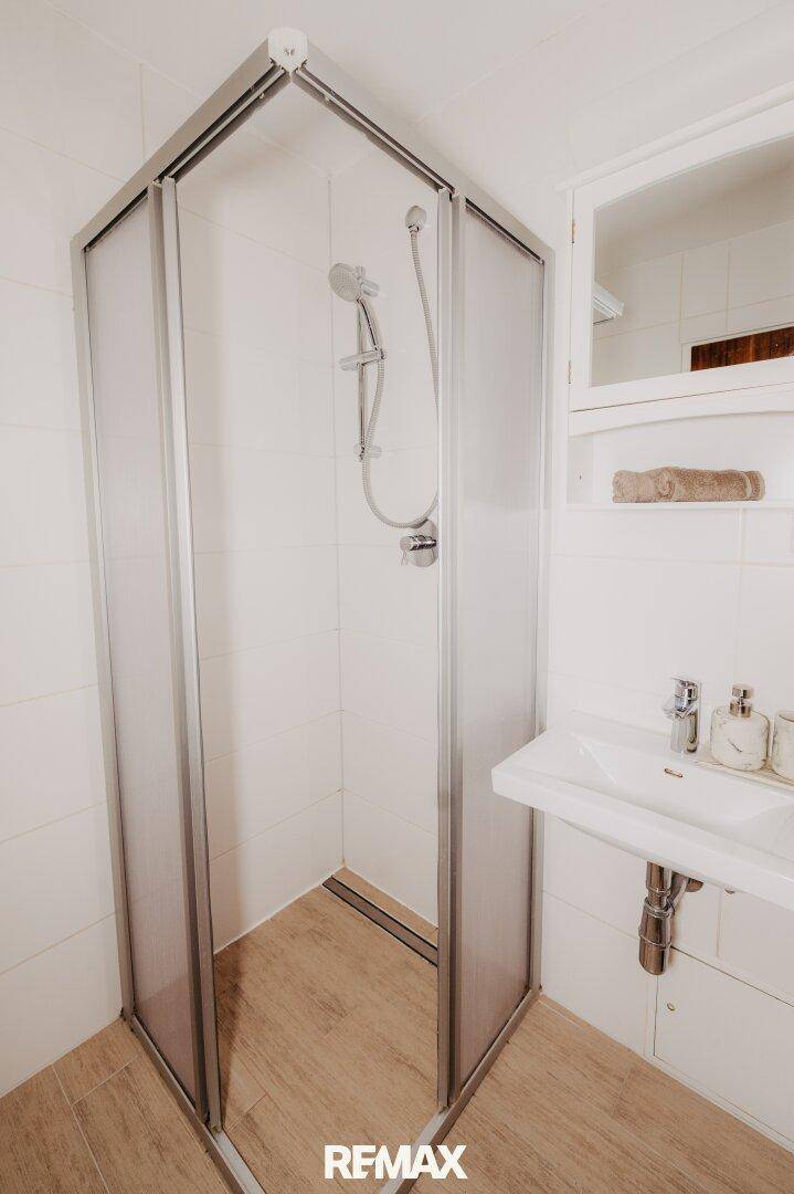Badezimmer mit Duschkabine, Waschbecken und Spiegelschrank, hell gefliest.