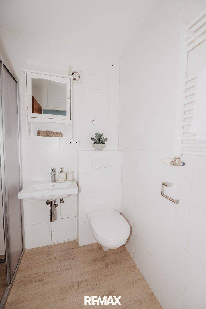 Helles Badezimmer mit WC, Waschbecken, Duschkabine und beheiztem Handtuchhalter.