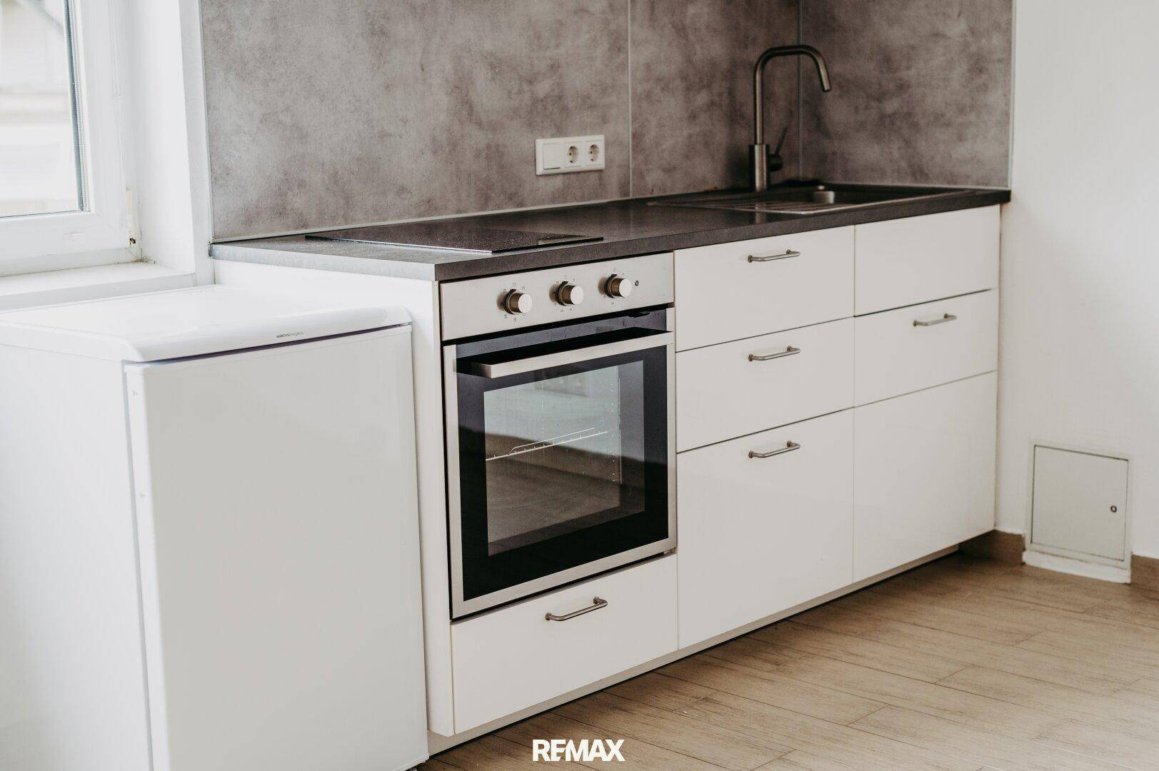 Kompakte Küchenzeile mit weißen Schränken, Backofen und Spüle, ideal für kleine Wohnungen.