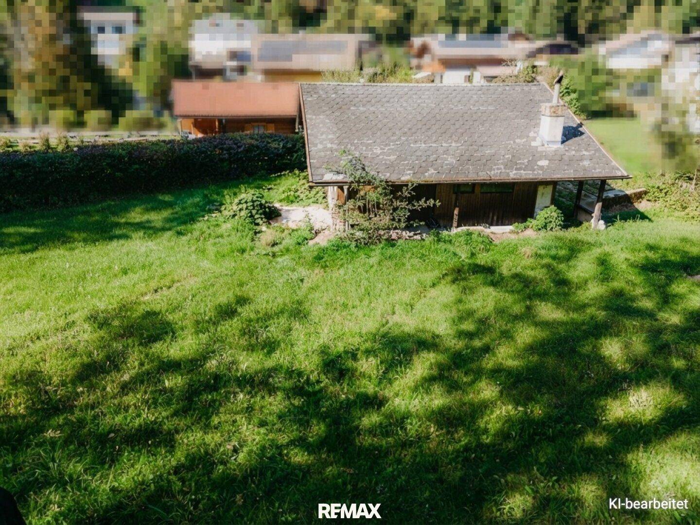 Kleines Haus mit grauem Dach und grünem Rasen, umgeben von einer ländlichen Landschaft mit weiteren Häusern.