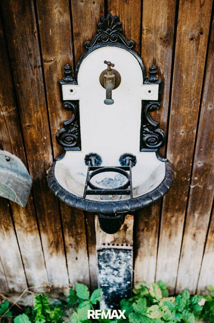 Detailansicht eines antiken Wasserhahns mit Waschbecken an einer rustikalen Holzwand.