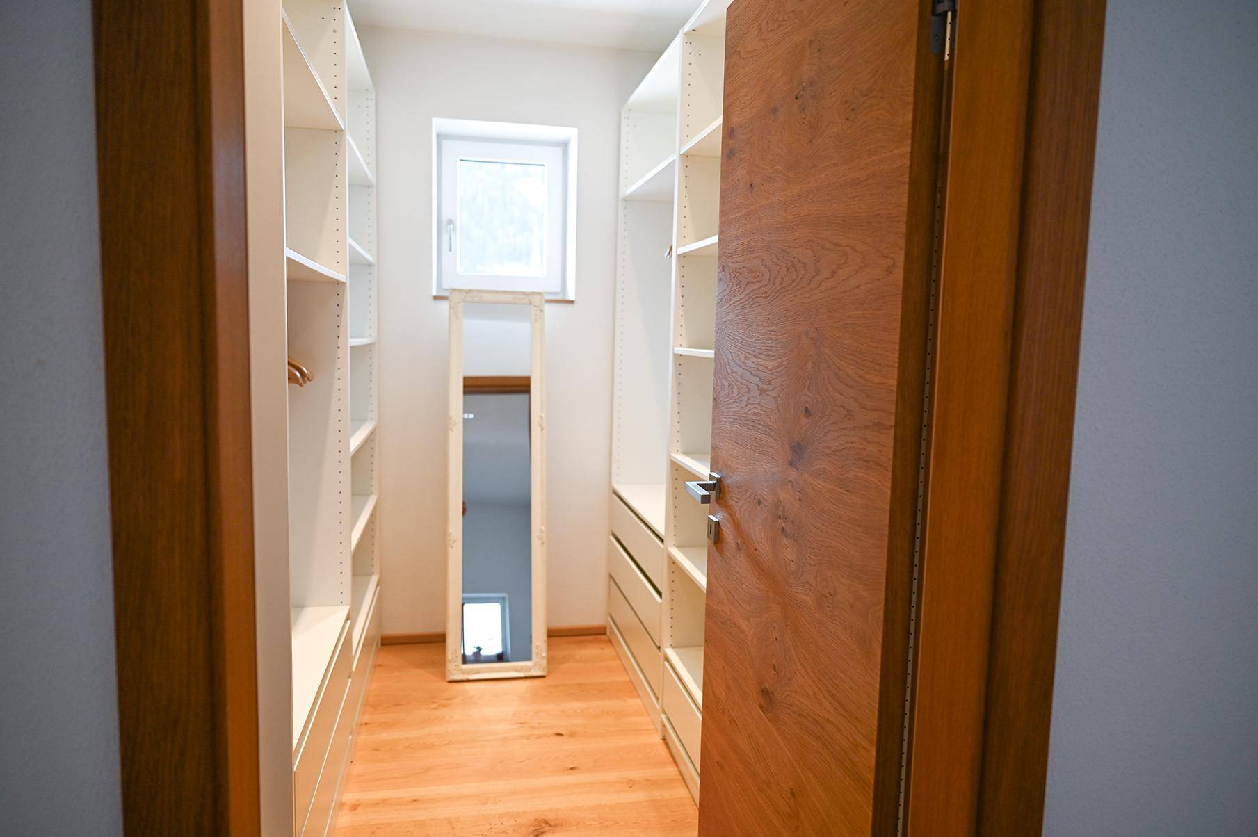 Praktischer begehbarer Kleiderschrank mit viel Stauraum und einem Fenster für Tageslicht.