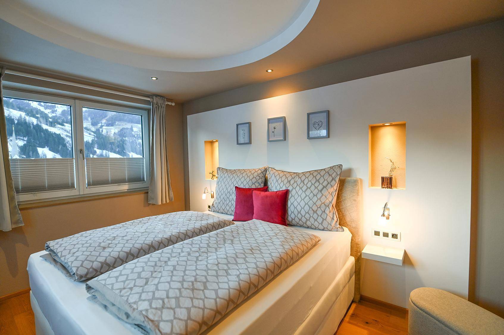 Elegantes Schlafzimmer mit Doppelbett, beleuchtetem Kopfteil und Fenster mit Bergblick.