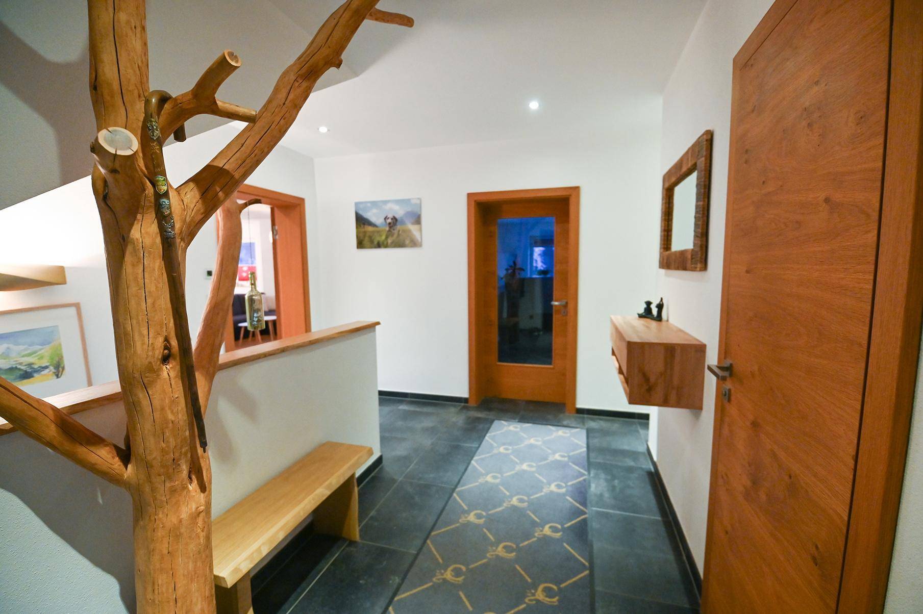 Eingangsbereich mit dunklen Fliesen, Holztüren, einer Sitzbank und dekorativem Holzelement.