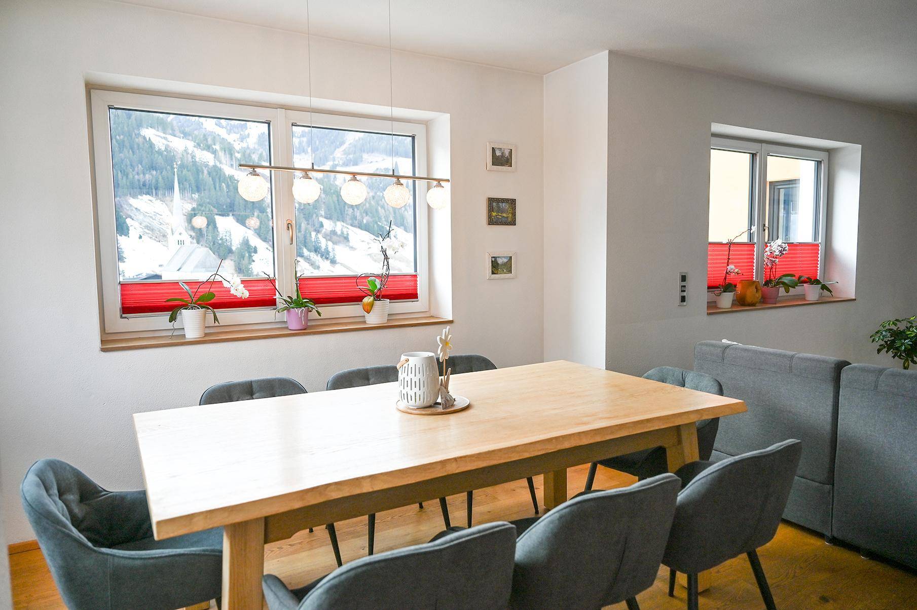 Heller Essbereich mit Holztisch, modernen Stühlen und weitem Blick auf die verschneiten Berge.