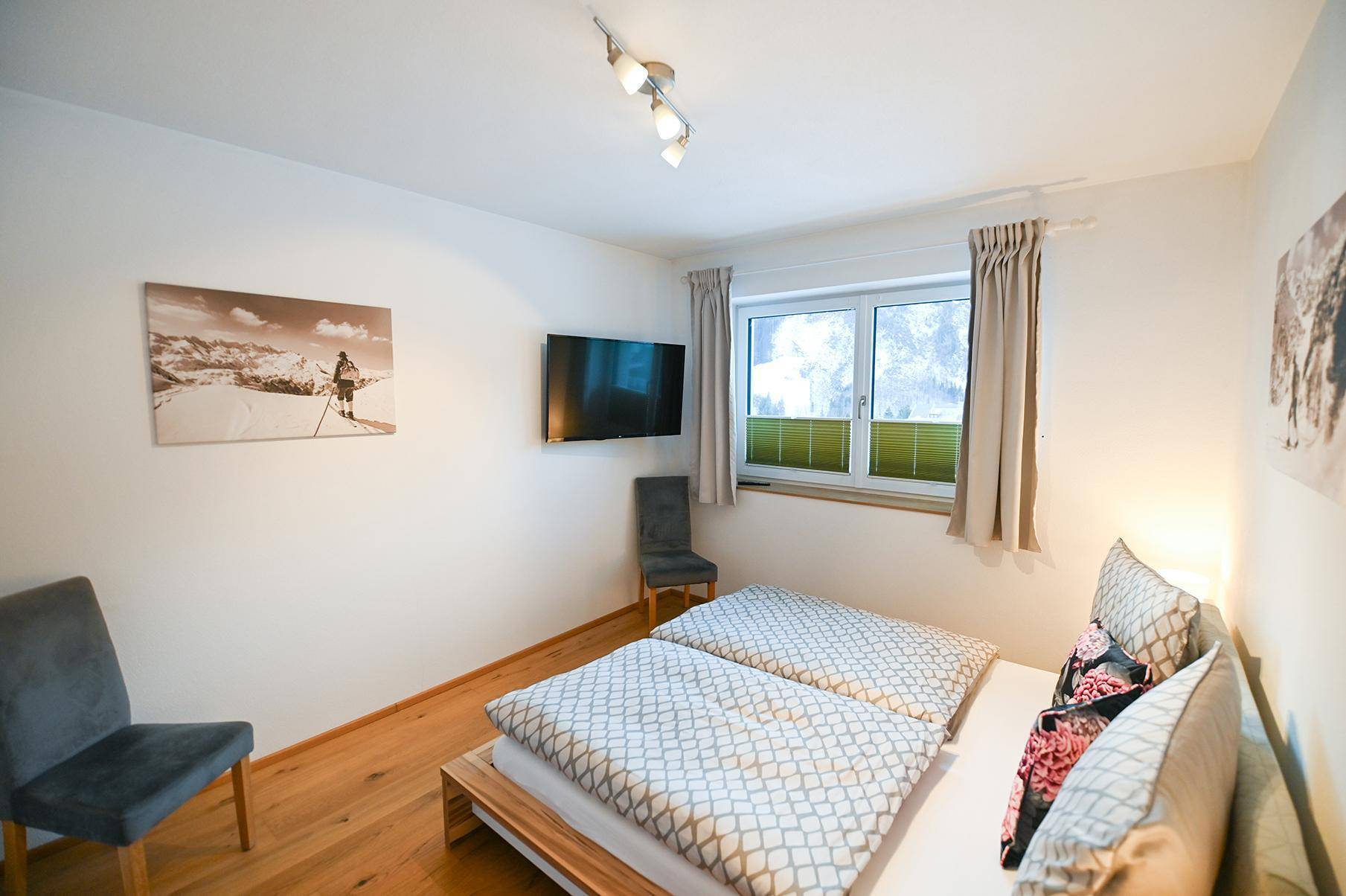 Komfortables Schlafzimmer mit Doppelbett, Wandfernseher und Fenster für angenehmes Licht.