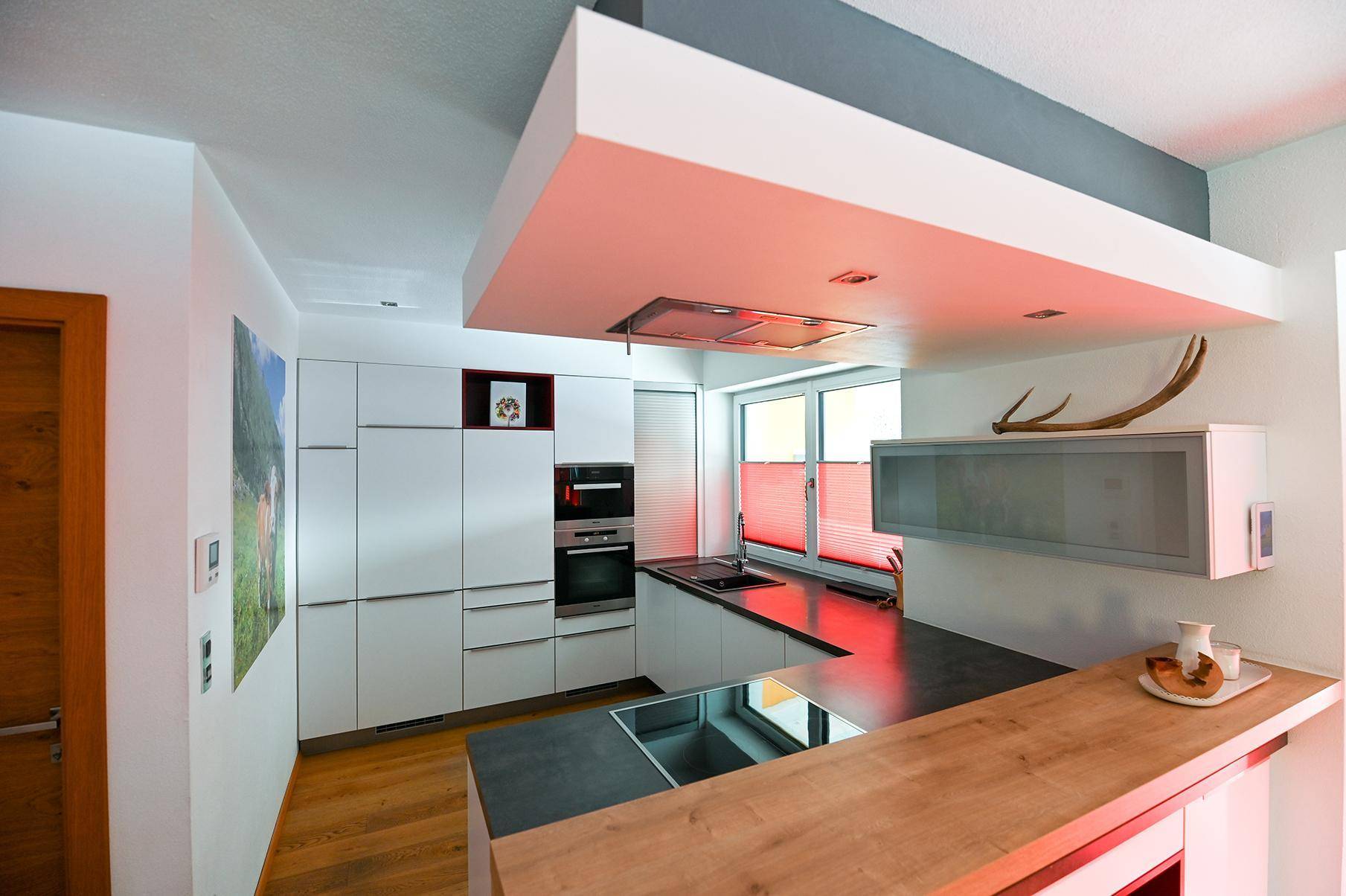 Moderne Küche mit weißen Schränken, dunklen Arbeitsplatten, integrierten Geräten und Frühstücksbar.