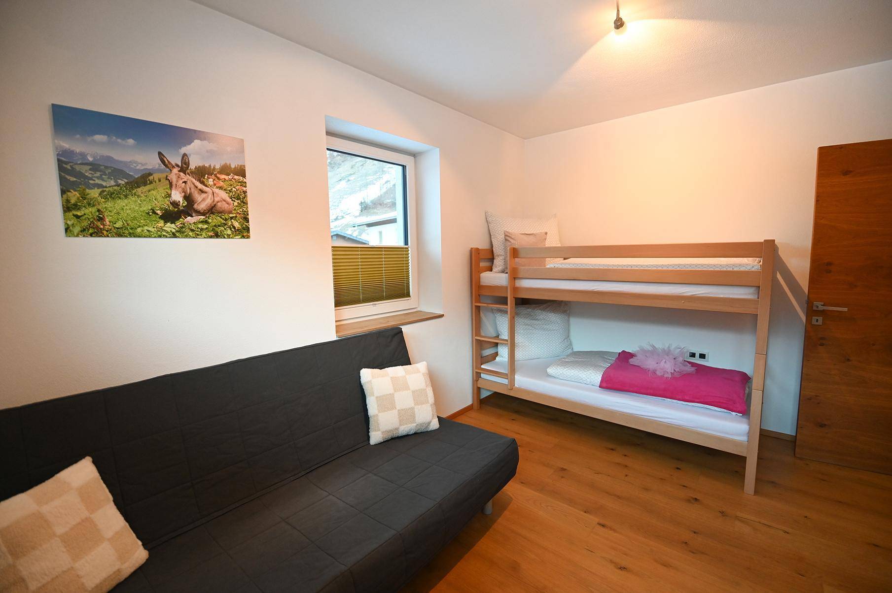 Helles Schlafzimmer mit Etagenbett, Schlafsofa und Fenster, bietet flexible Schlafmöglichkeiten.