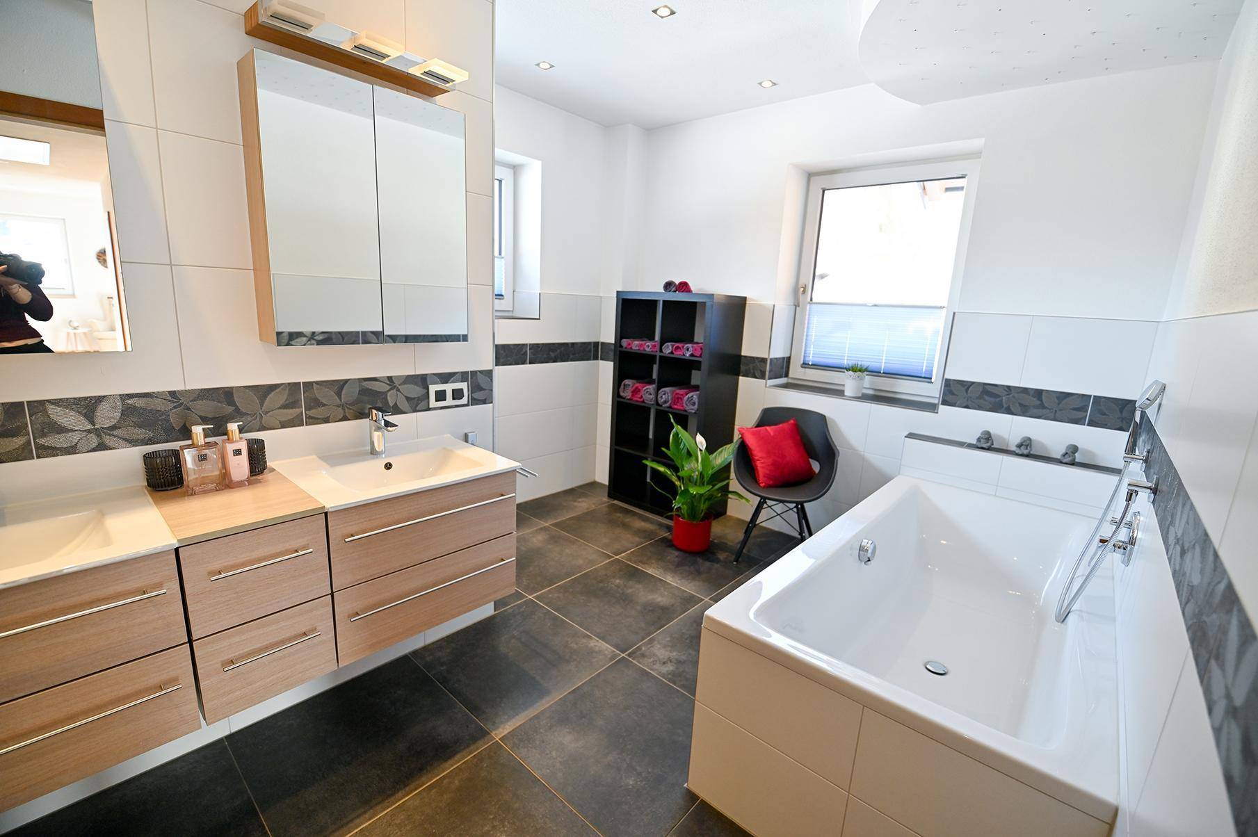 Modernes Badezimmer mit Badewanne, Doppelwaschbecken, dunklen Fliesen und Fenster.