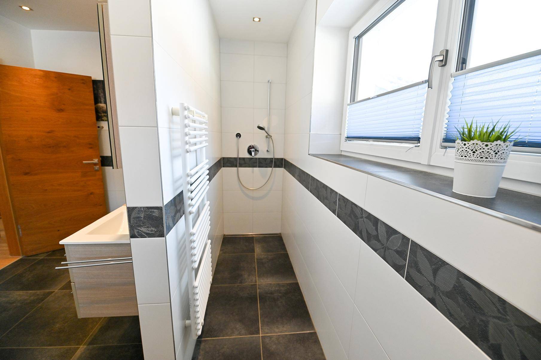 Geräumige Dusche im Badezimmer mit modernen Fliesen, Handtuchheizkörper und Fenster.