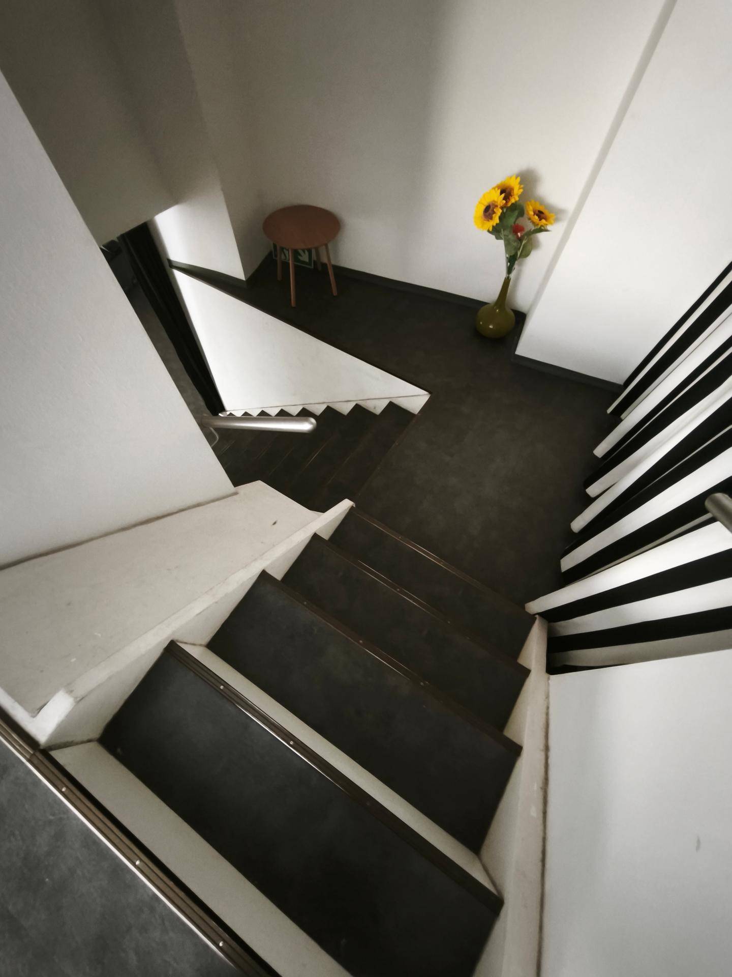 Treppenhaus mit dunklen Stufen, weißen Wänden und einem Blumenstrauß als Dekoration.