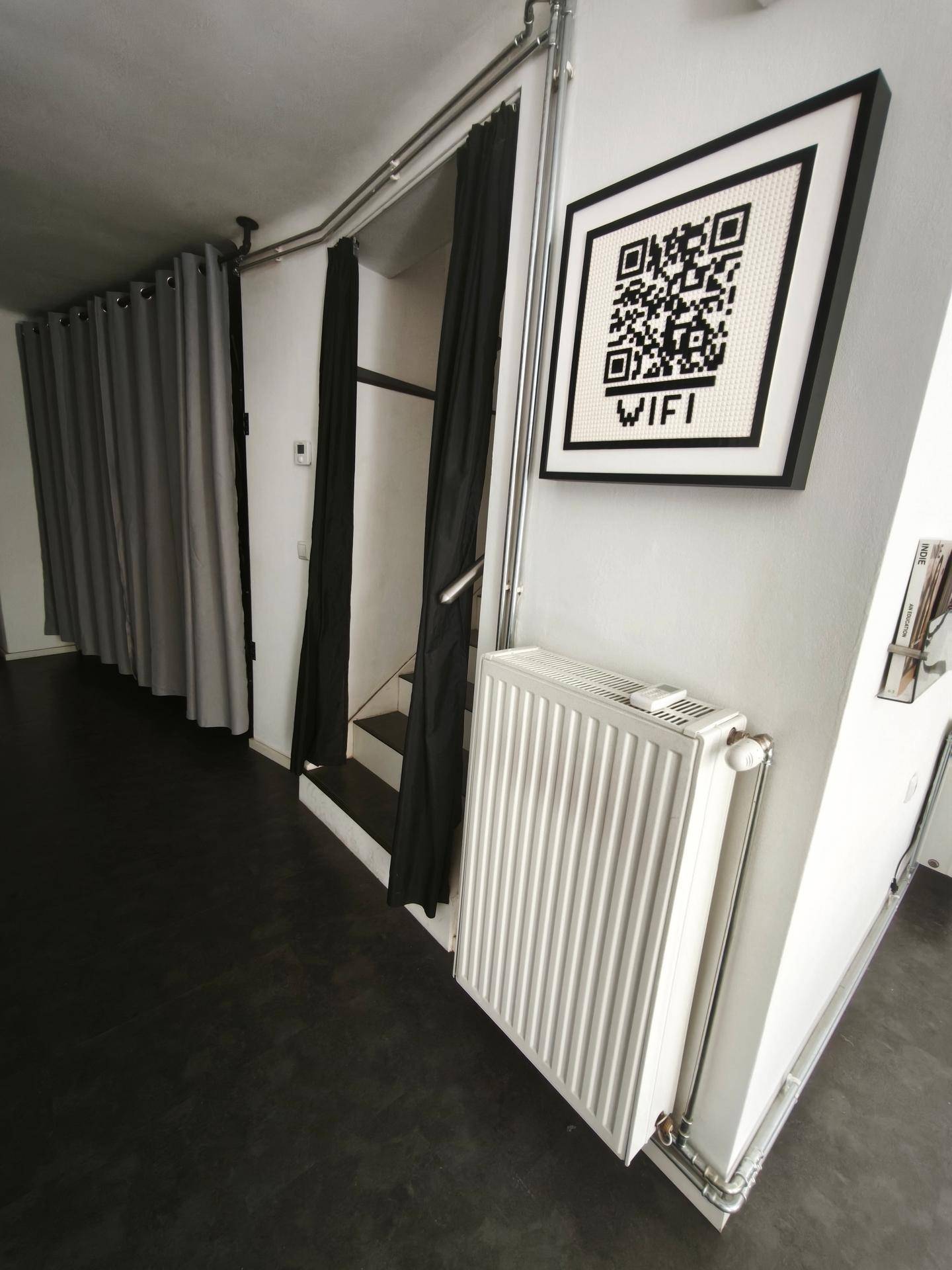 Flur mit Heizkörper, Vorhängen und einem gerahmten QR-Code für WLAN-Zugang.