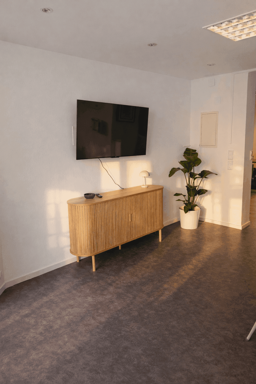 Heller Bürobereich mit einem an der Wand montierten Fernseher und einem Sideboard aus Holz.