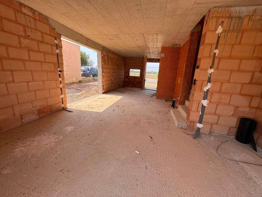 Innenansicht eines Raumes im Rohbau mit Ziegelwänden und Betonboden, bereit für den Ausbau.