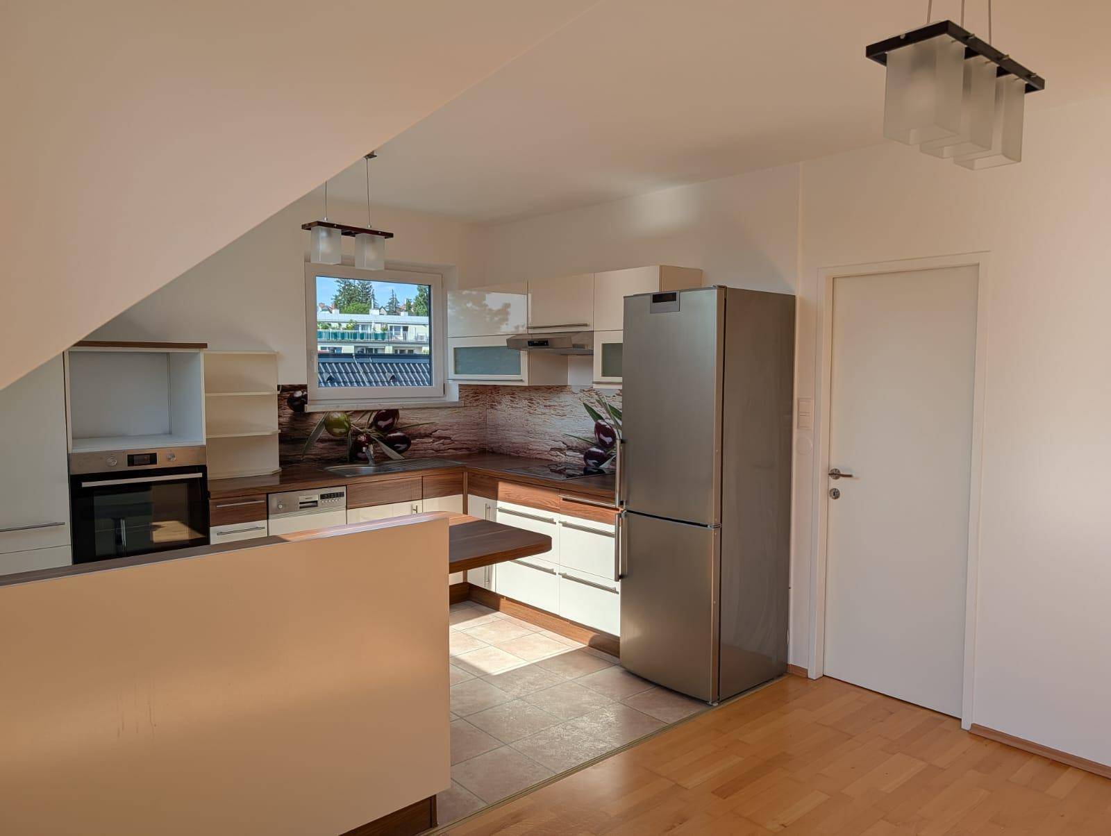 Funktionale Küche in Dachgeschosswohnung mit modernen Geräten und hellem Fliesenboden.