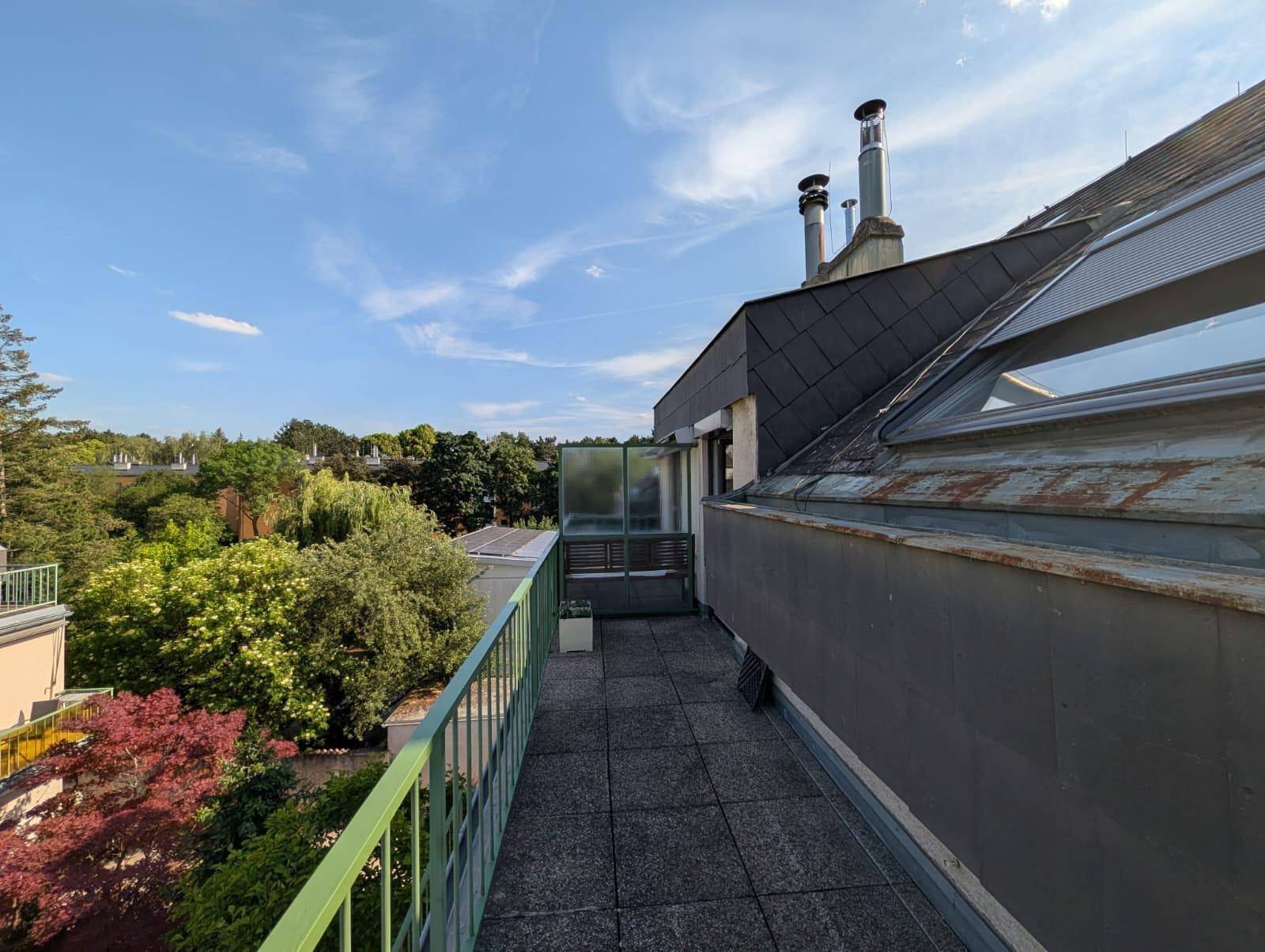 Langer Balkon mit grüner Brüstung und Ausblick auf die umliegenden Gebäude und Bäume.