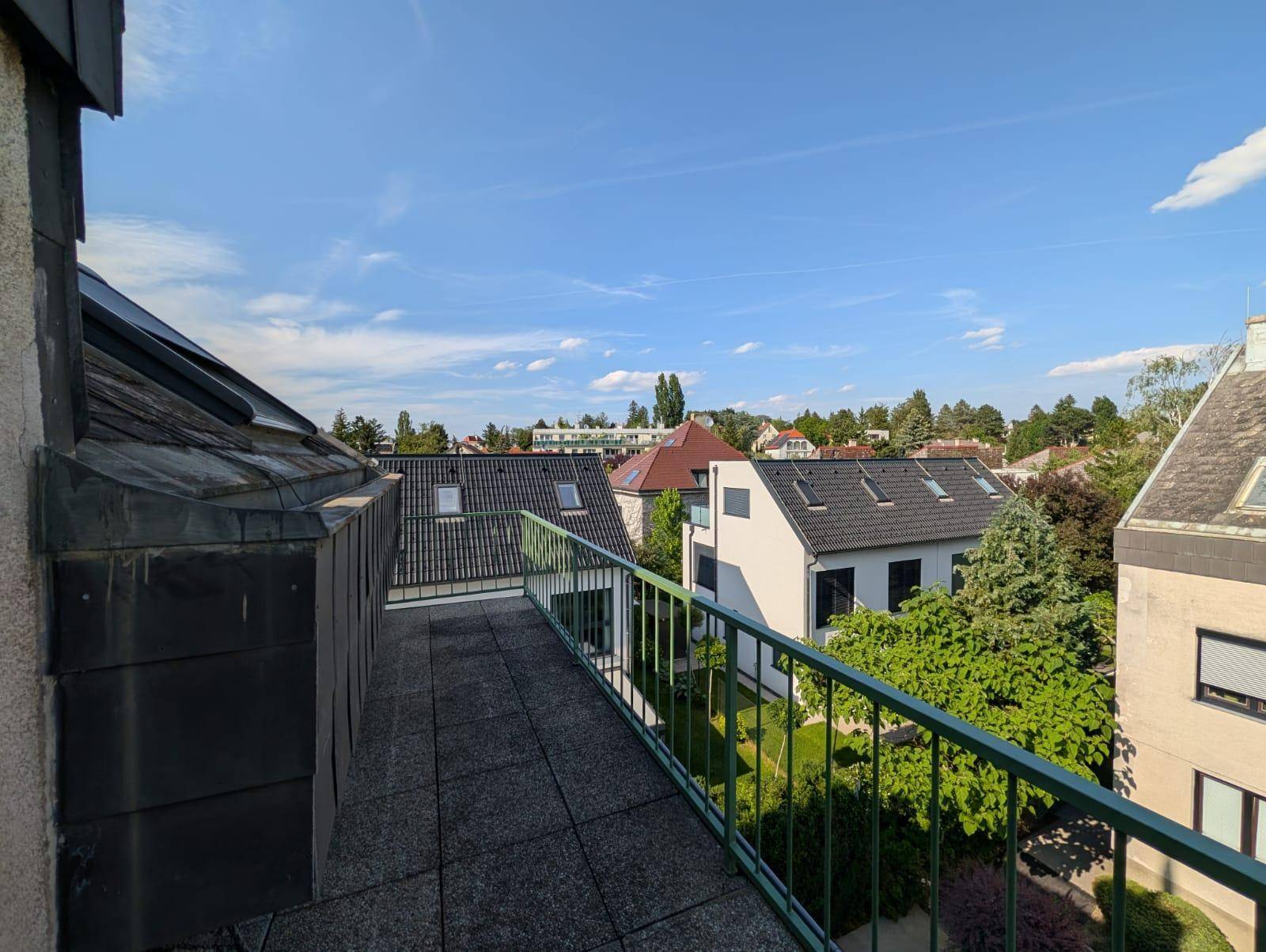 Weitläufiger Balkon mit Blick über die Dächer und grüne Umgebung.