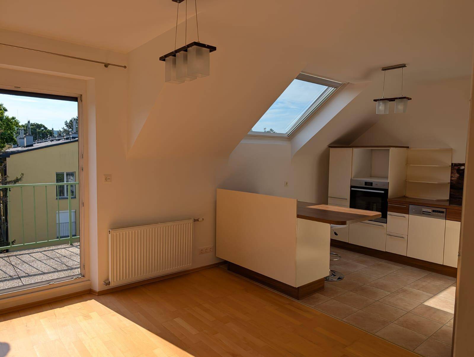 Heller offener Wohnbereich mit Holzboden, Dachfenster und Zugang zum Balkon.