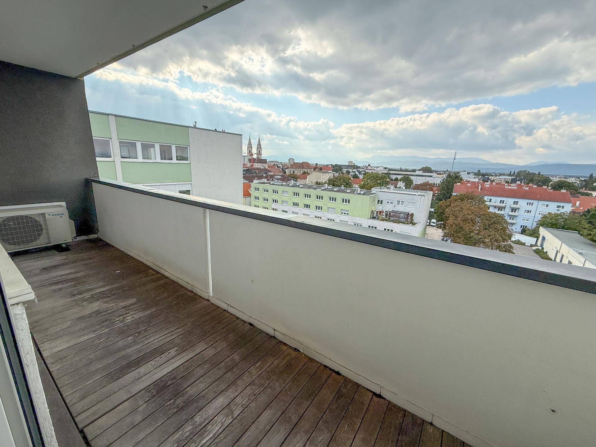 Balkon mit Holzboden und weitem Blick über die Stadt bis zu den Bergen.
