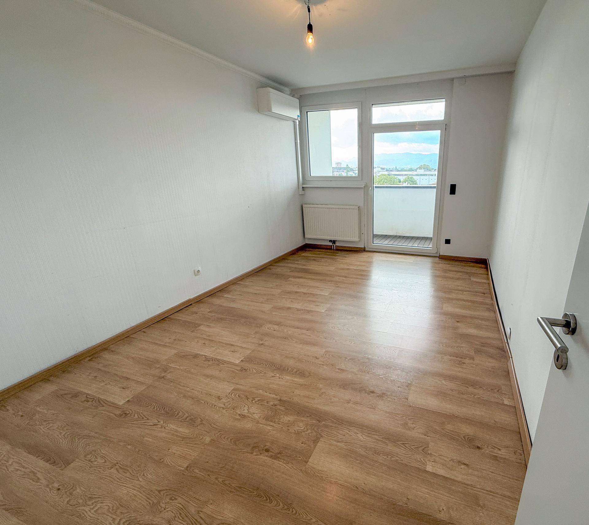 Helles Schlafzimmer mit Holzboden und Zugang zu einem Balkon.
