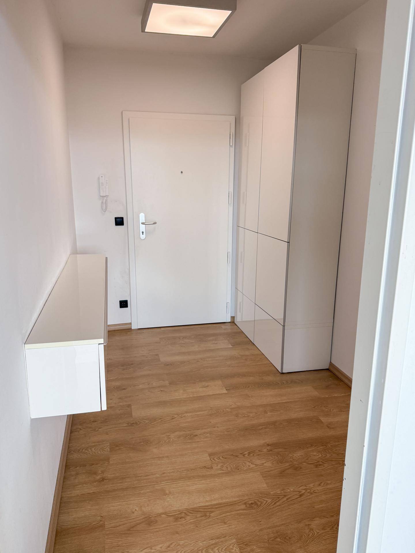 Heller Eingangsbereich mit Holzboden, weißem Schrank und schwebendem Regal für Ablage.